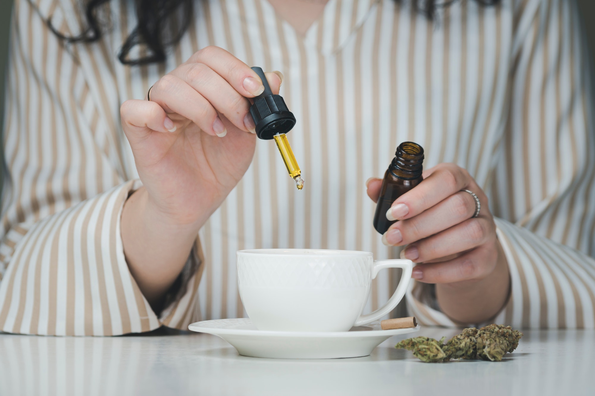 Close-up of female hand holding pipette with cbd oil, dripping into coffee mugs