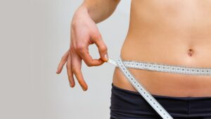 Young woman measuring her waistline in a gym with a tape